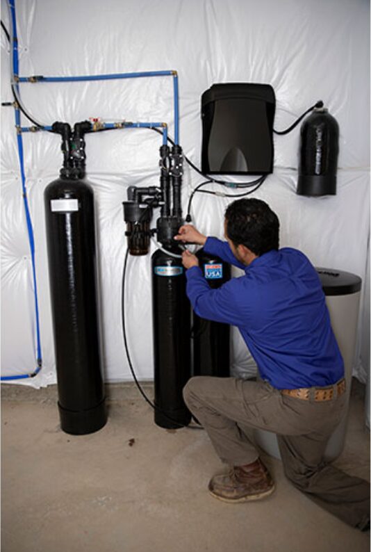 Cardinal Water technician kneeling beside a newly installed softener in a basement