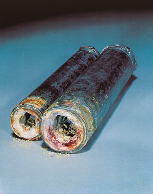 Two old water pipes cut open, their openings narrowed by mineral scale